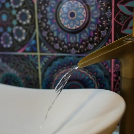 Das elegante Aufsatz-Waschbecken wird von einer Retro-Messing-Wasserfall-Armatur ergänzt, die einen Hauch von Luxus verleiht.